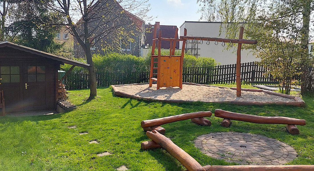 Ein Außenbereich mit grünem Rasen, Holzstämmen und einem Spielplatz.