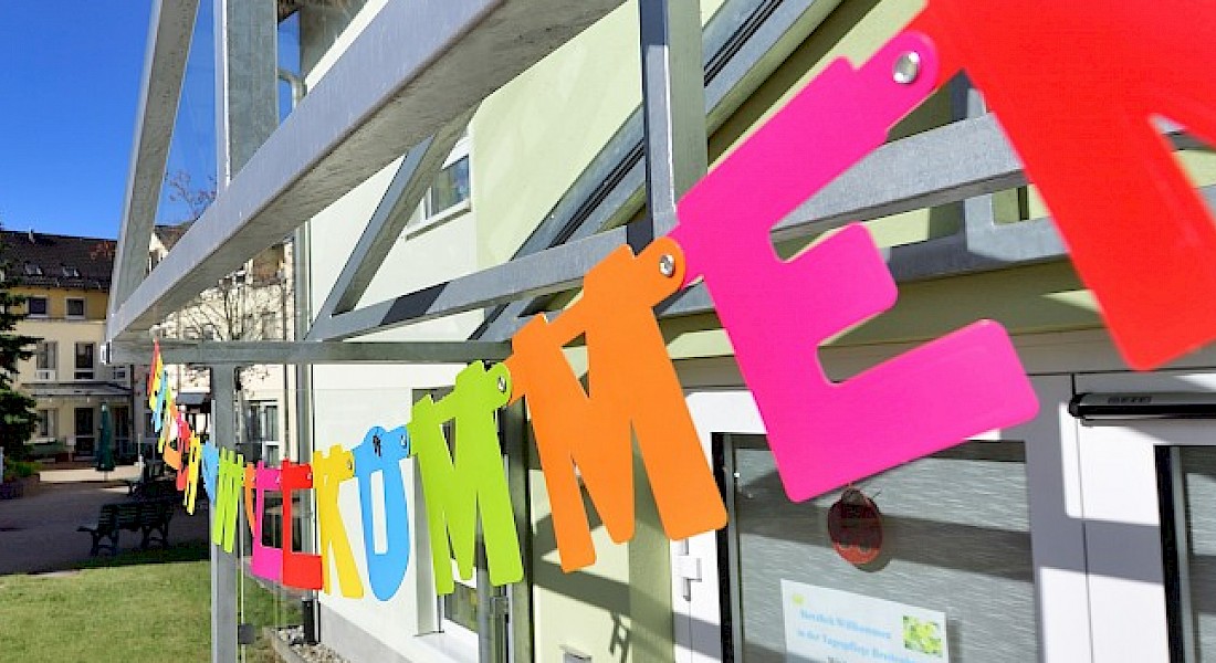 Bunte Buchstaben hängen als Wimpelkette vor einem Gebäude