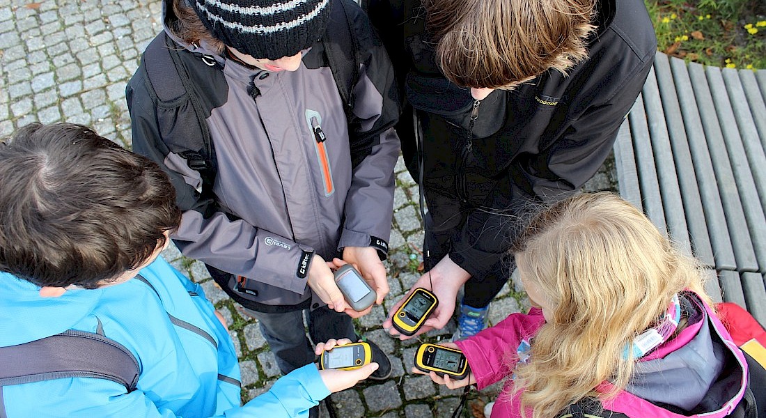 Vier Jugendliche halten GPS-Geräte bei einer Schnitzeljagd in den Händen.