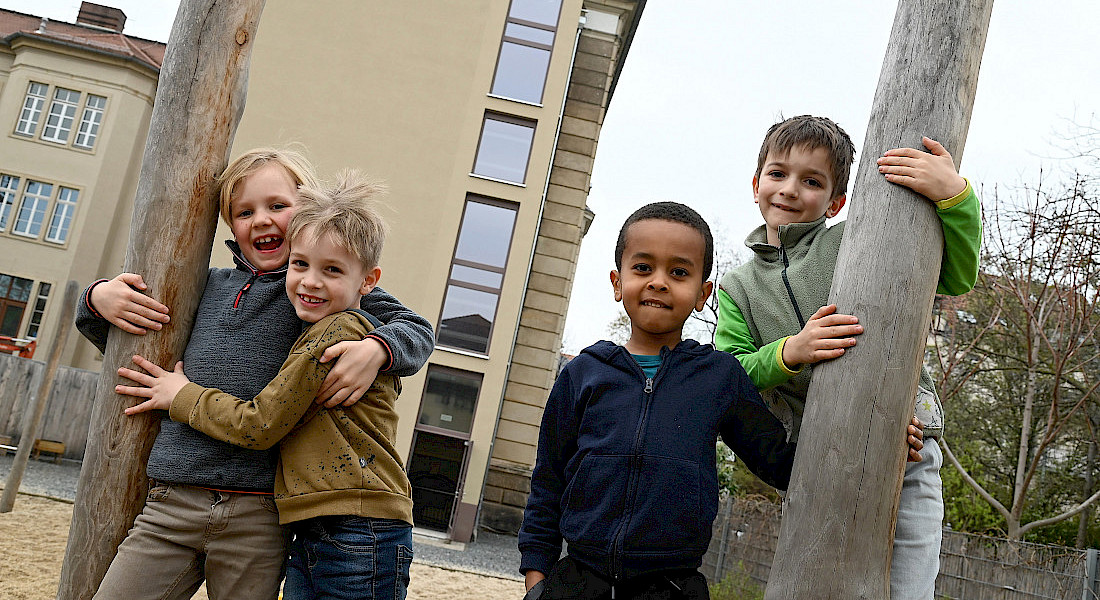 Vier Kinder stehend lachend auf einem Spielplatz.