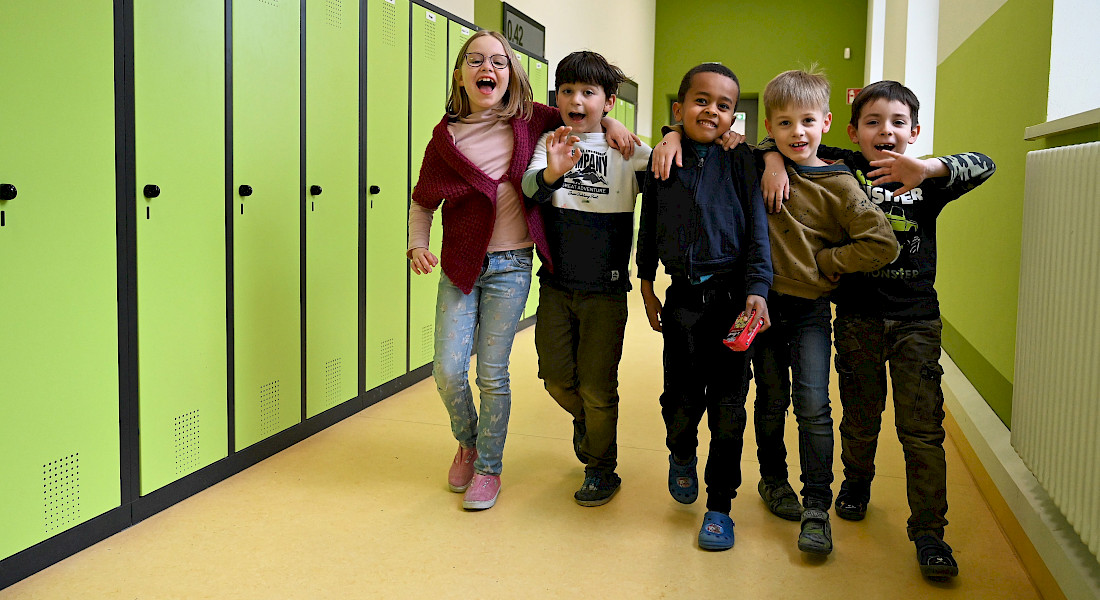 Eine Gruppe Kinder läuft fröhlich durch einen Flur mit grünen Spinden.