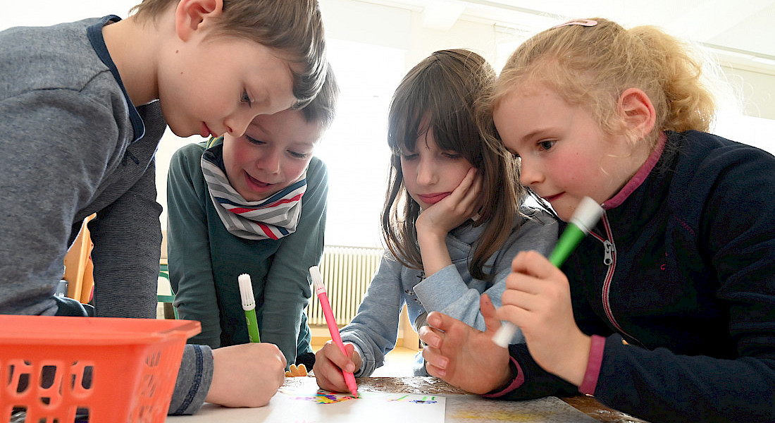 Mehrere Kinder schreiben und zeichnen gemeinsam an einem Tisch.