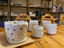 Mehrere weiße Vasen und Gefässe stehen auf einem Holztisch