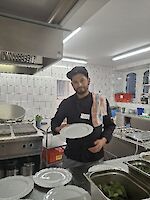 Person in schwarzer Kochkleidung in der Küche beim Anrichten.