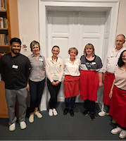 Ein Gruppe lächelt in die Kamera, einige tragen rote Schürzen.