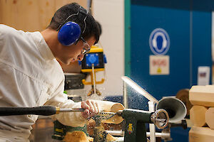 Klient bearbeitet an der Drechselbank ein Stück Holz mit seinem Werkzeug.