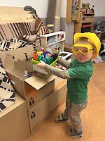 Kind mit Bauhelm und Schutzbrille packt Kiste für Kita-Umzug