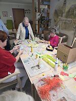 Mehrere Personen basteln an Tisch mit Zeitungen ausgelegt