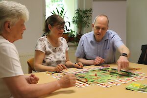 Drei Personen am Tisch spielen Brettspiel