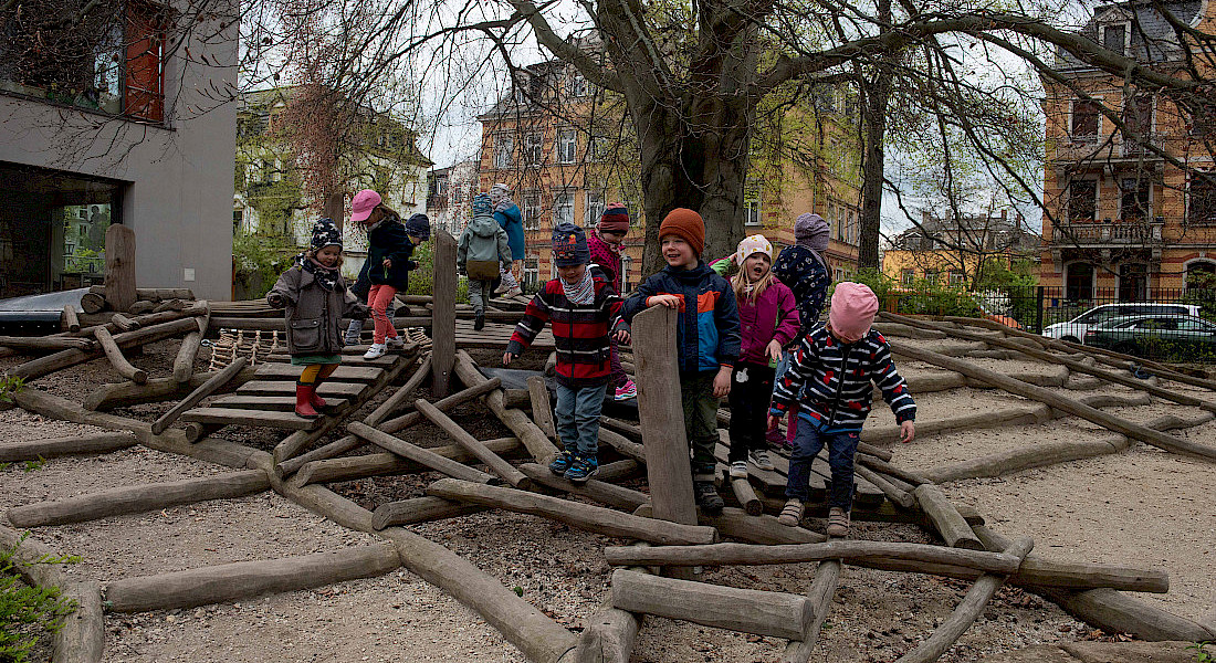 Kinder klettern und balancieren auf einer Holzspielanlage im Garten der Kita.