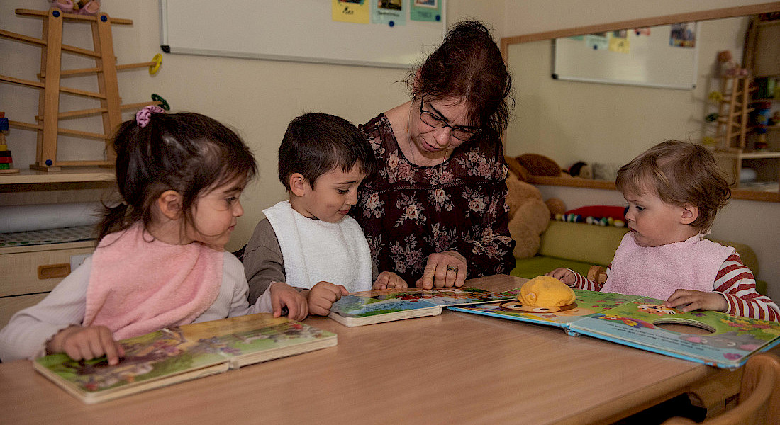 Eine Erzieherin schaut mit drei kleinen Kindern gemeinsam Bilderbücher an.