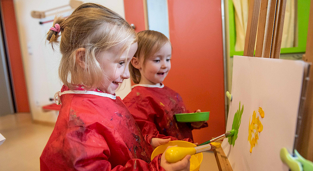 Zwei Kinder malen mit Pinseln an einer großen Staffelei in der Kita.