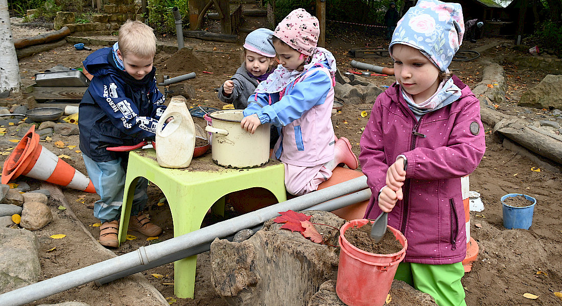 Vier Kinder spielen im Garten mit Sand und Wasser an einer Matschstation.