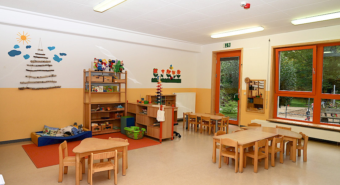 Ein Gruppenraum mit Tischen, Stühlen und Spielmaterialien.