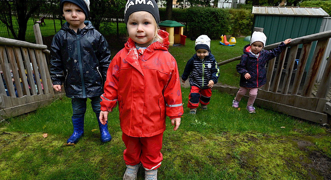 Vier Kinder stehen im Garten und tragen wetterfeste Kleidung.