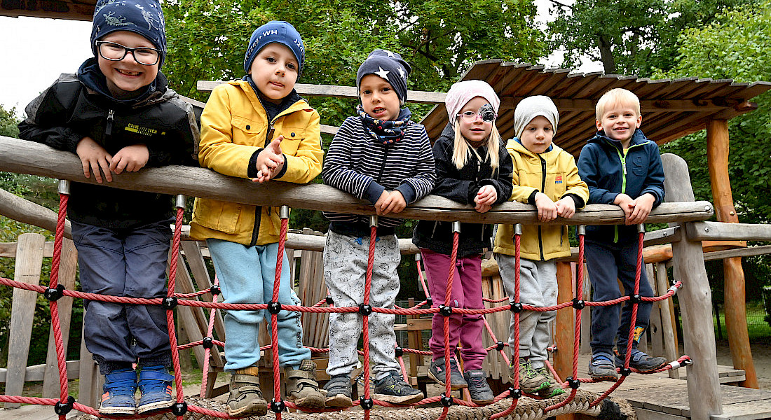 Mehrere Kinder stehen nebeneinander auf einer Hängebrücke im Außengelände.