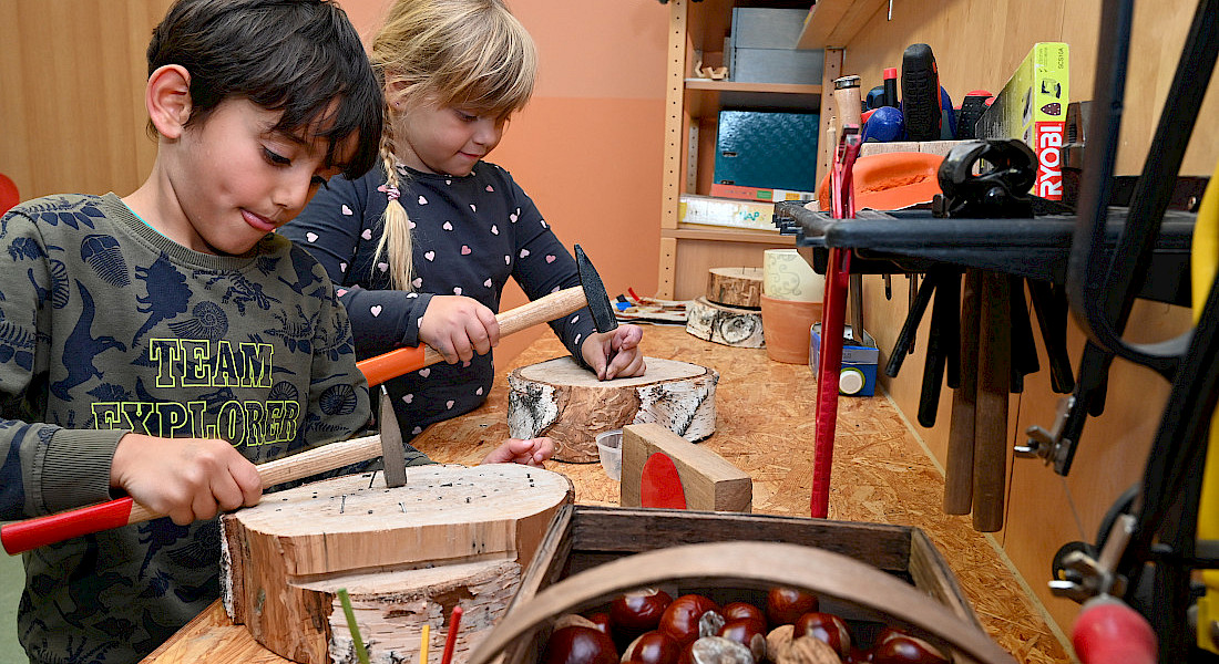 Zwei Kinder arbeiten mit Naturmaterialien und Werkzeug an einem Tisch in der Kita.