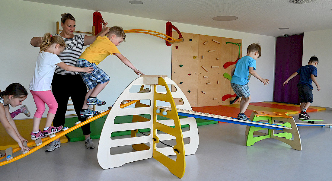Kinder balancieren auf Spielgeräten im Bewegungsraum der Kita.