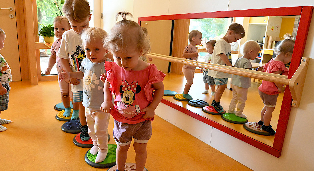 Mehrere Kleinkinder balancieren im Bewegungsraum auf Wackelelementen.