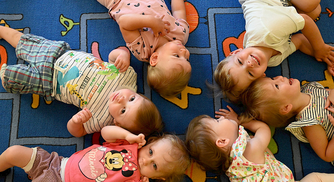 Kinder liegen gemeinsam auf dem Teppich in einem Gruppenraum.