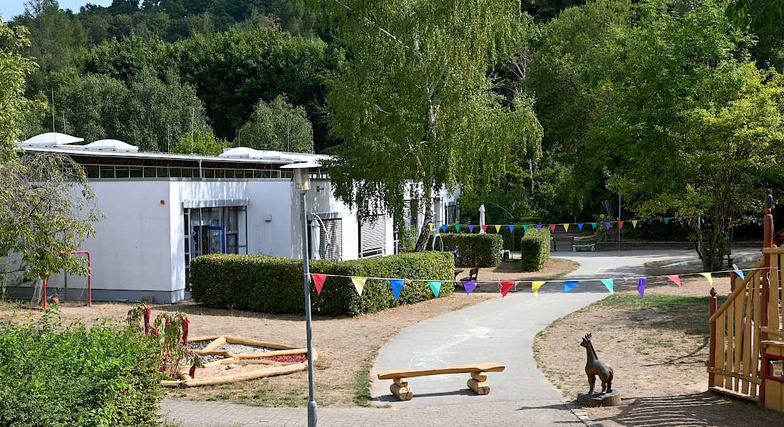 Ein gepflasterter Weg mit aufgemalter Fahrbahn führt durch das Außengelände einer Kita.