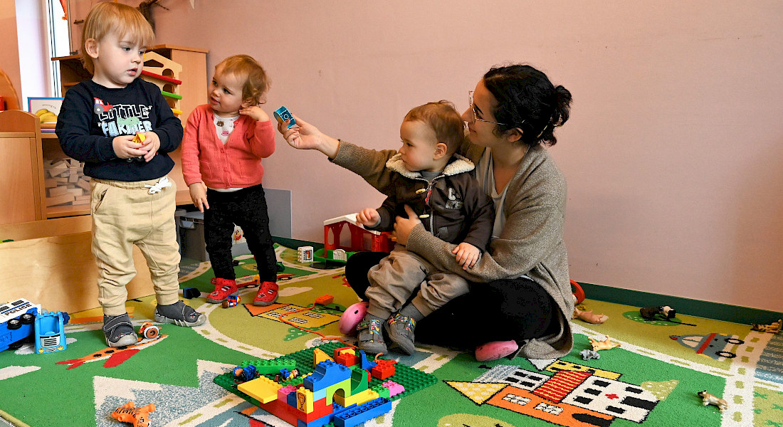 Kleinkinder und eine erwachsene Person sitzen auf einem Teppich und spielen mit Klemmsteinen.