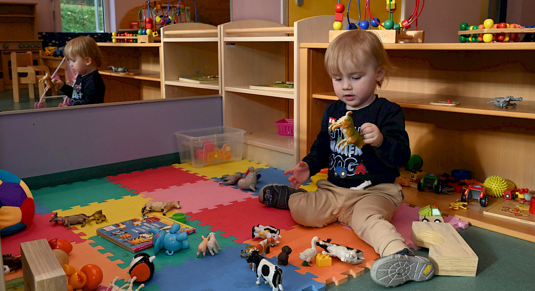 Ein Kleinkind sitzt auf einer bunten Schaumstoffmatte und spielt mit Tierfiguren.