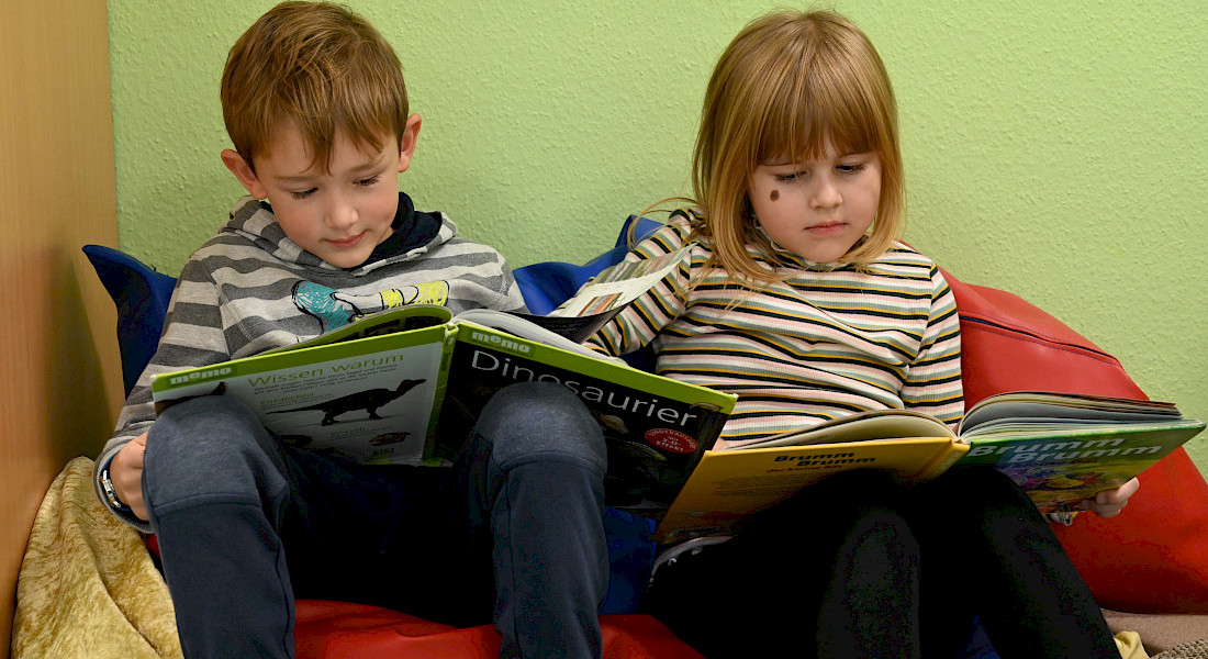 Zwei Kinder sitzen nebeneinander und blättern in einem Buch.