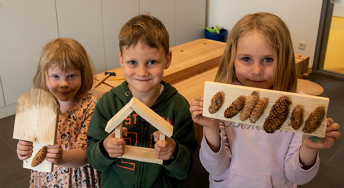 Drei Kinder halten gebastelte Werkstücke in die Kamera.