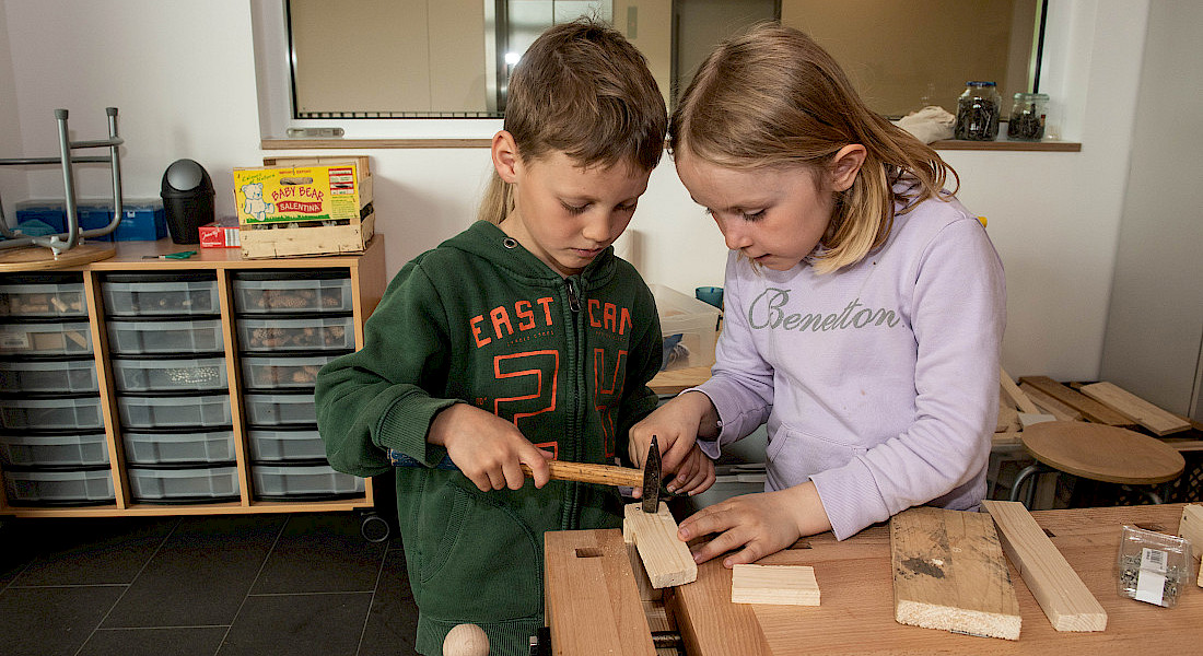 Zwei Kinder arbeiten gemeinsam mit Hammer und Holz an einer Werkbank.