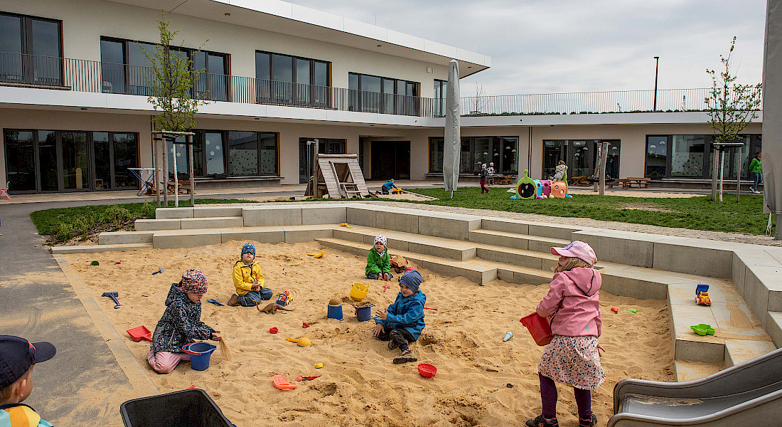 Mehrere Kinder spielen mit Förmchen und Eimern im großen Sandkasten der Kita.