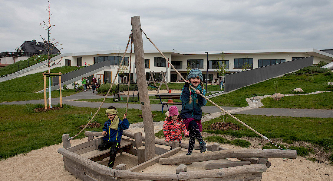 Kinder balancieren und spielen auf einem Holzschiff im Außengelände.