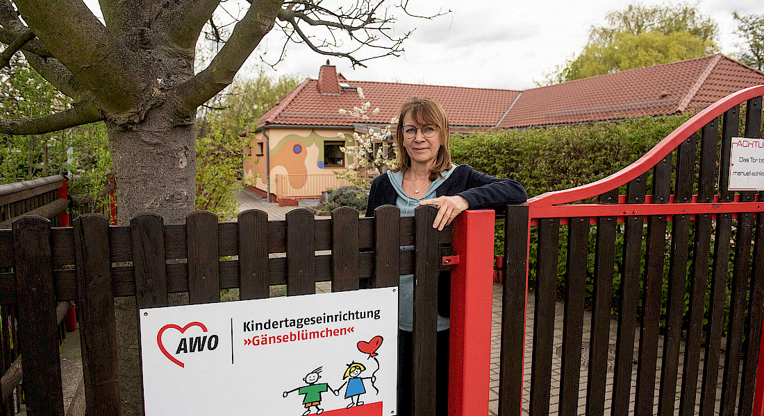 Eine Person steht am Gartentor neben einem Schild der AWO Kindertageseinrichtung.