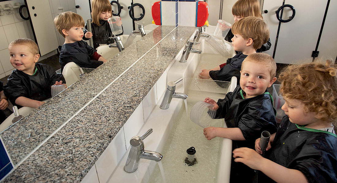 Kinder waschen sich die Hände an einem langen Waschbecken.