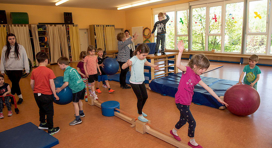 Kinder balancieren in einem Bewegungsraum über eine schmale Bank.