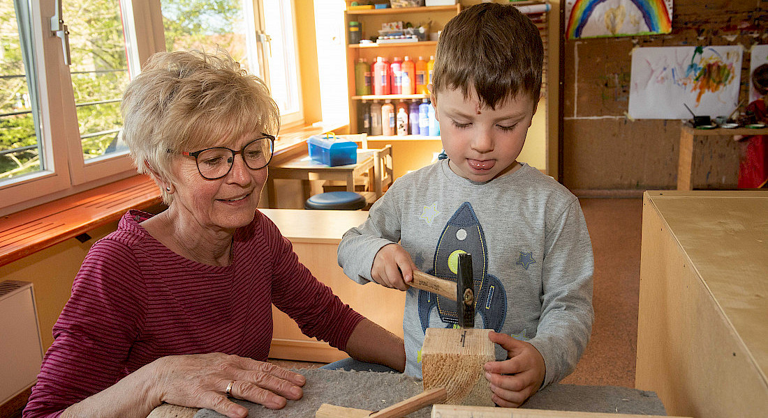 Eine erwachsene Person unterstützt ein Kind beim Arbeiten mit Holz.