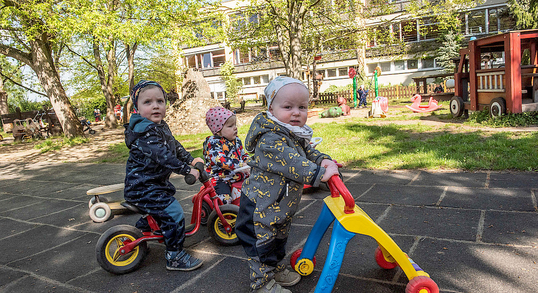 Mehrere Kleinkinder fahren mit kleinen Fahrzeugen auf einem Spielplatz.