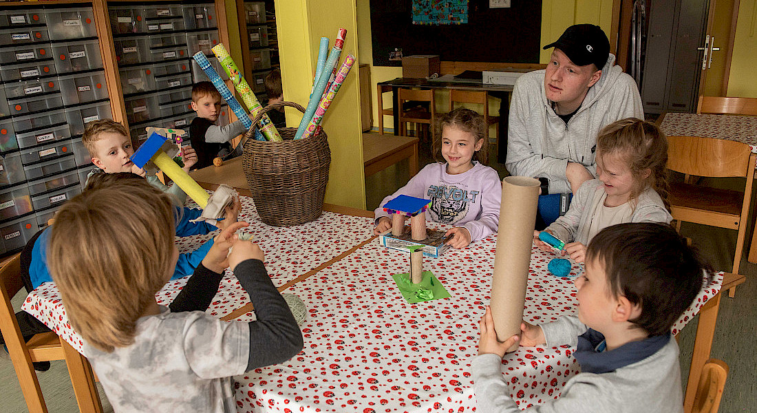 Kinder sitzen um einen Tisch und experimentieren mit bunten Röhren.