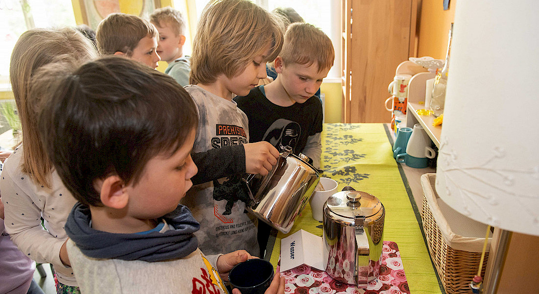 Kinder füllen Getränke in Tassen.