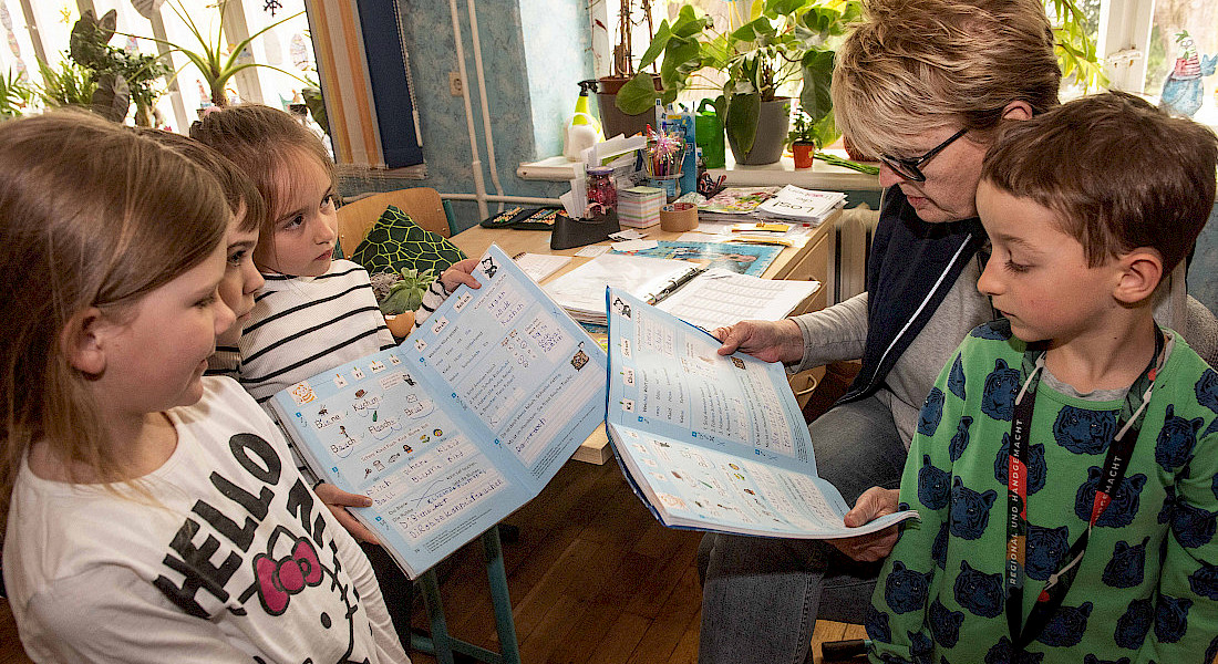 Kinder schauen sich gemeinsam mit einer erwachsenen Person ein Buch an.