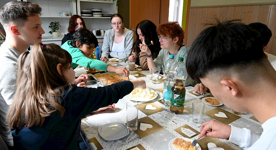 Jugendliche und Erwachsene sitzen gemeinsam an einem gedeckten Tisch und essen.