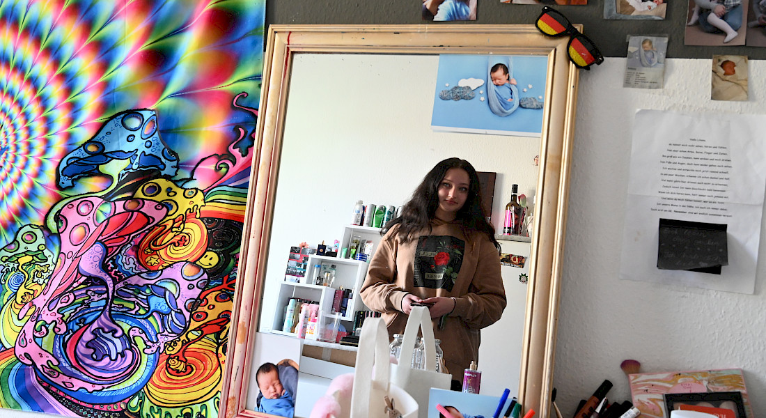 Eine Jugendliche fotografiert sich in einem Spiegel in einem bunt dekorierten Zimmer.