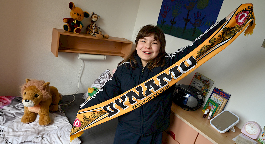 Eine Jugendliche hält lächelnd einen Fanschal von Dynamo Dresden.