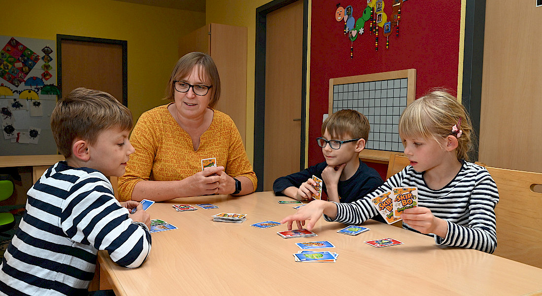Kinder und eine erwachsene Person spielen ein Kartenspiel am Tisch.
