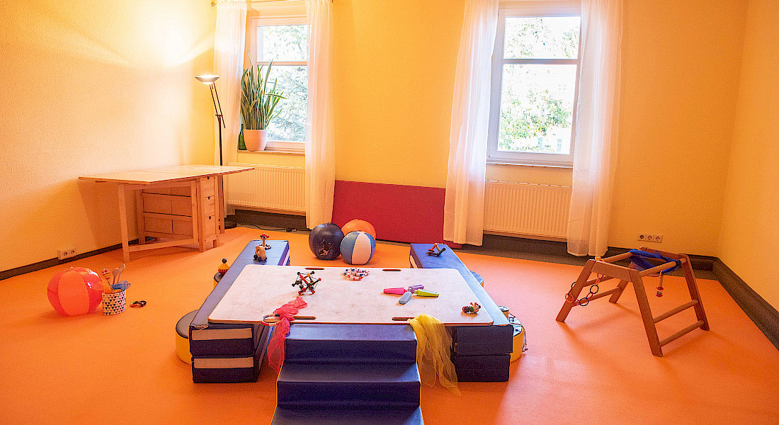 Blick in einen hellen Raum mit verschiedenen Spielelementen für Babys auf dem Boden.