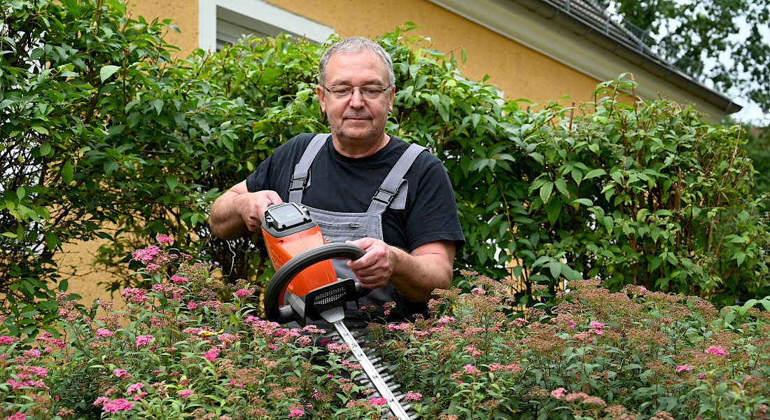 Ein Hausmeister schneidet eine Hecke.