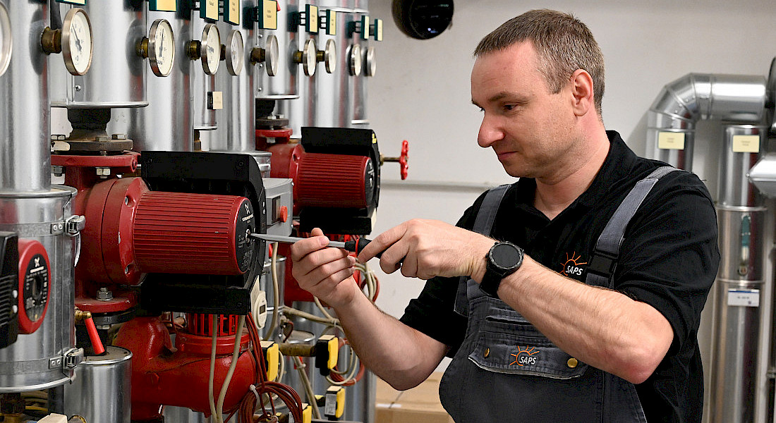 Ein Handwerker schraubt an einem Rohrsystem.