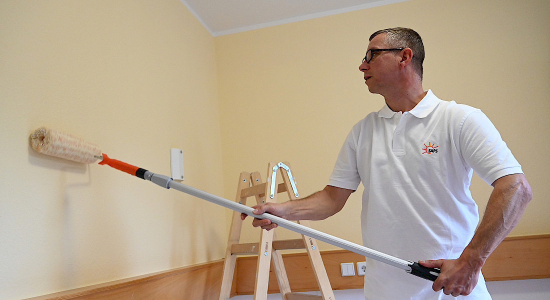 Ein Handwerker malert mit einer Rolle eine Wand.