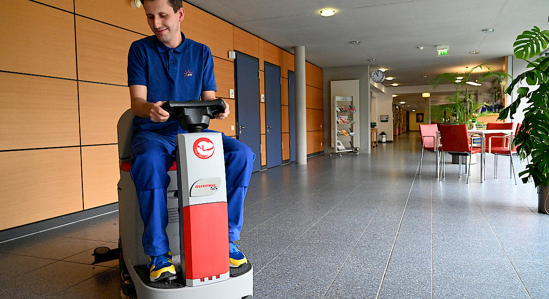 Eine Reinigungsfachkraft säubert den Boden mit einer Maschine.