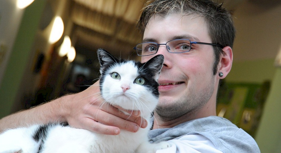 Eine Person lächelt und hält eine schwarzweiß gefleckte Katze im Arm.